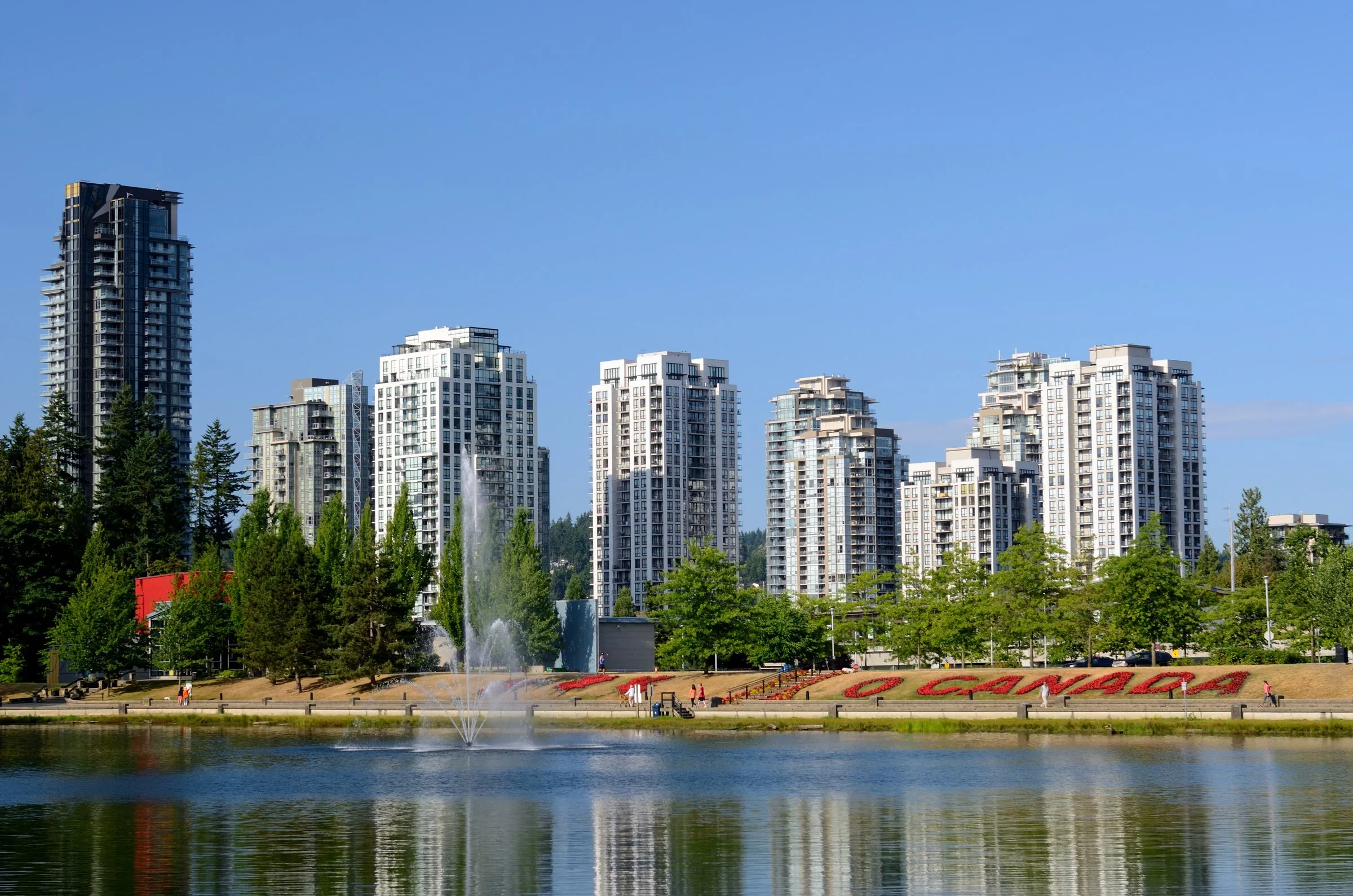 Lafarge Lake with a fountain in front of tall residential towers in Coquitlam on a clear summer day.