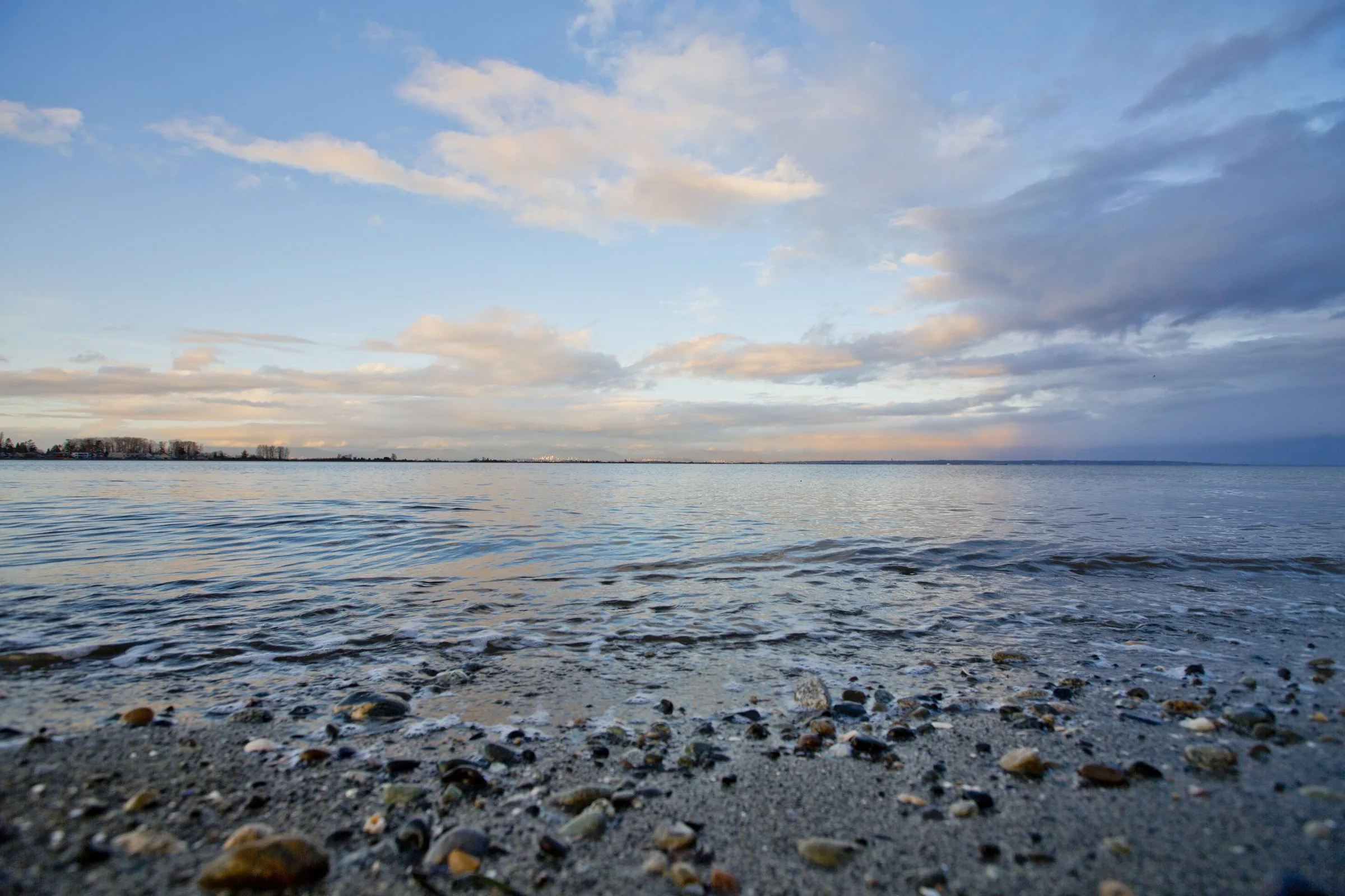 Gentle waves on a pebble beach at Boundary Bay in Tsawwassen under a wide sky of soft clouds.