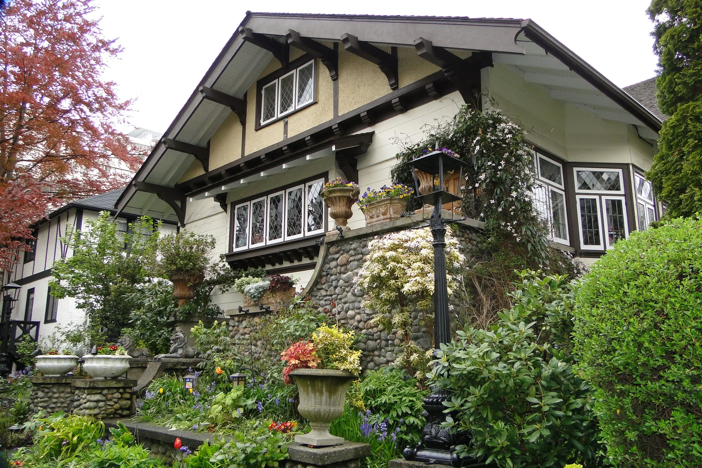A craftsman style house above a stone wall and a colourful spring garden in Kitsilano, Vancouver.